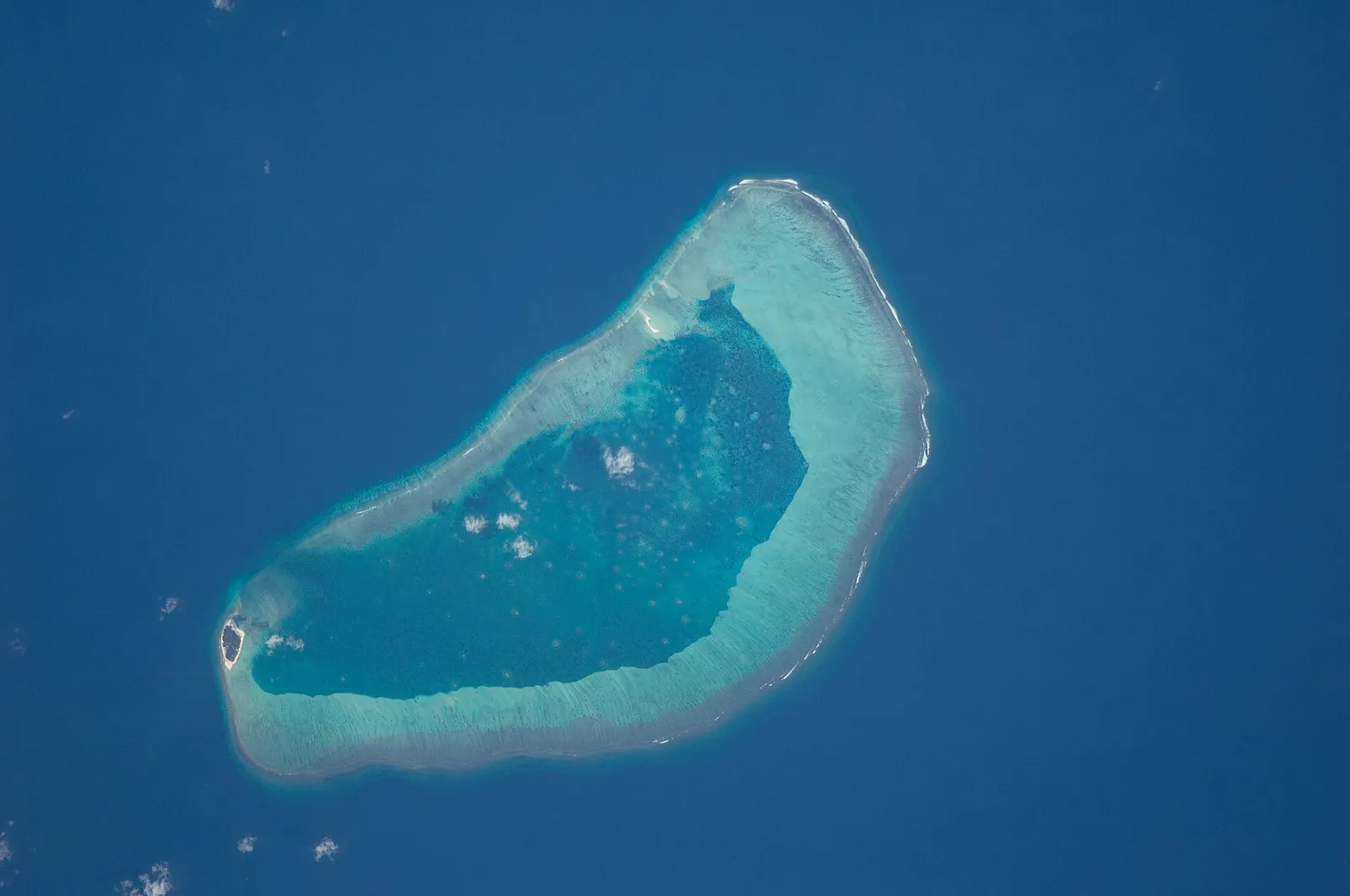 Oval coral atoll with a turquoise lagoon inside a reef ring, surrounded by deep blue ocean